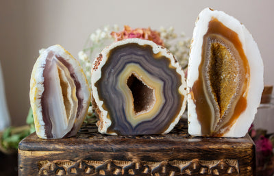 Three cut base agates displayed in a row on a wooden box. Colors vary from blue to brown and vary slightly in size.