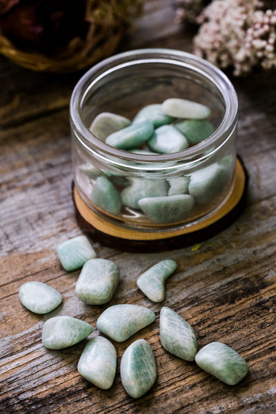 Glass jar filled with green-blue tumbled stone with loose stones on the table surrounding. 