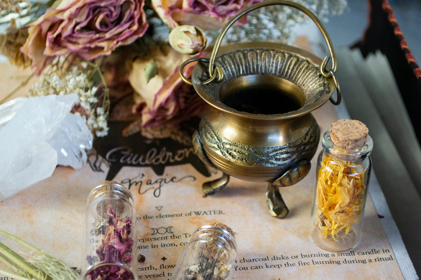 Small brass cauldron displayed with flowers and herb vials. 
