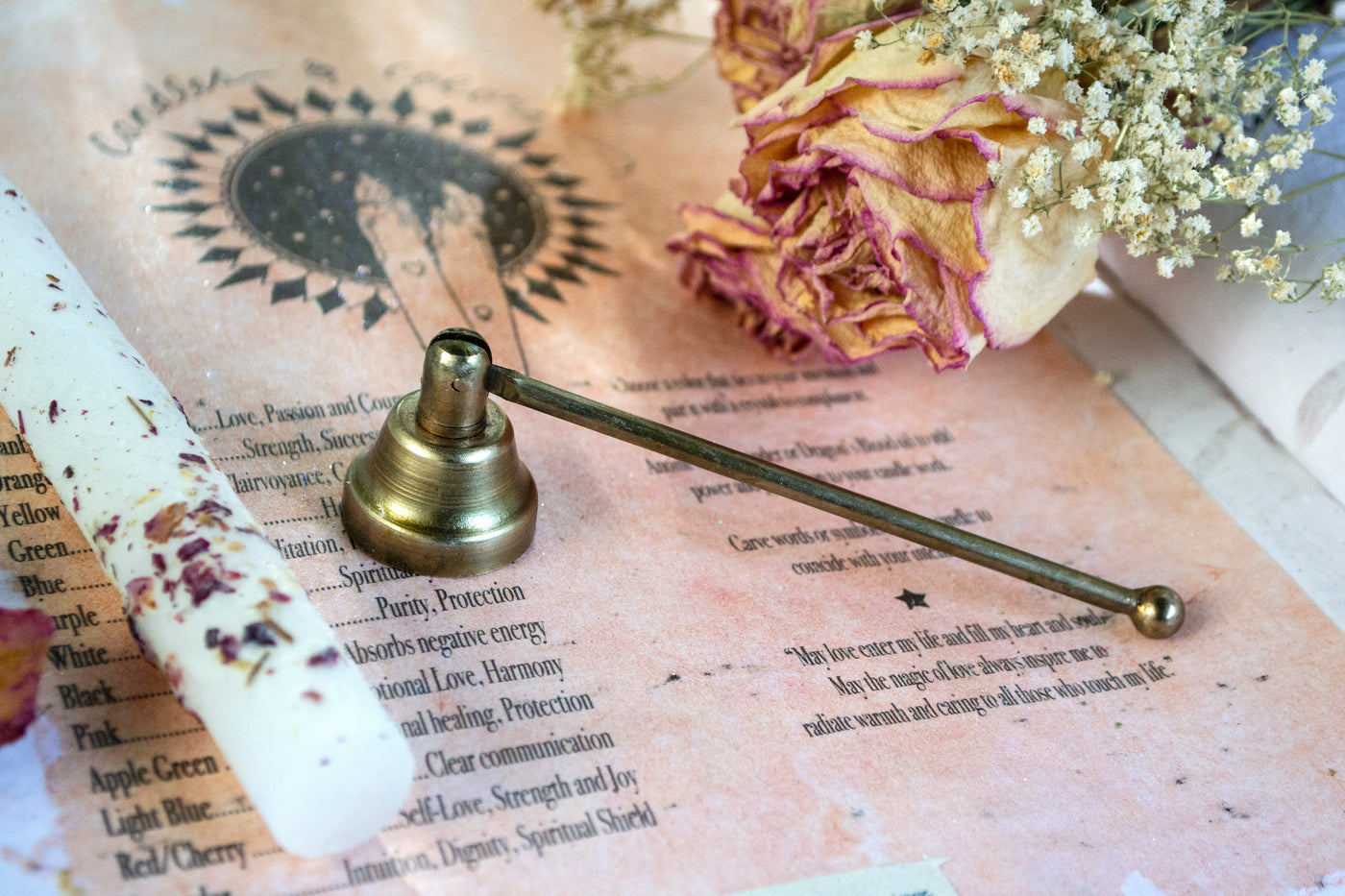 Brass candle snuffer next to a floral infused candle. 